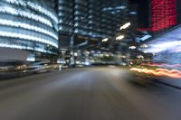 a city street is lit up with lights at night time and blurry cars drive down the road