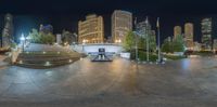 a fisheye lens view of the city at night with buildings and walkways with people sitting in the benches