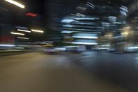 blurred view of a street at night showing cars passing by and skyscrapers in the background