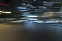 blurred view of a street at night showing cars passing by and skyscrapers in the background