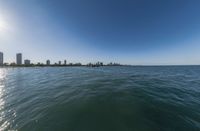 a view of the city from a boat in the ocean with a sun shining on it