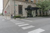 two men walk in front of an apartment building across from a red stop sign on the street