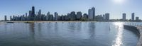 city skyline across the water from park on a sunny day by lake shore with sun in center