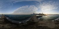 a fish eye view of the water with some buildings in the background, and there's a boat out on the ocean