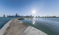 a wide body of water near a city with buildings behind it and sun in the sky