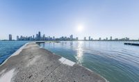 a wide body of water near a city with buildings behind it and sun in the sky