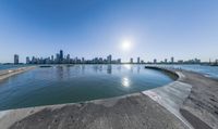 a wide body of water near a city with buildings behind it and sun in the sky