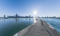 a wide body of water near a city with buildings behind it and sun in the sky