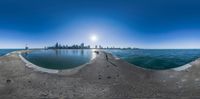 the view from a cement fence, of a city and a sea water, as well as the reflection of the sun