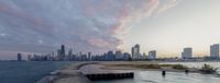 the city skyline is in view of the water at sunset time as people watch from a pier