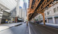 a street in a big city is lined with lots of buildings, including an overpass that overlooks a parking garage