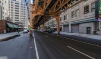 a street in a big city is lined with lots of buildings, including an overpass that overlooks a parking garage