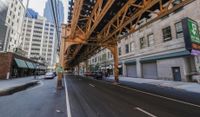 a street in a big city is lined with lots of buildings, including an overpass that overlooks a parking garage