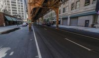 a street in a big city is lined with lots of buildings, including an overpass that overlooks a parking garage