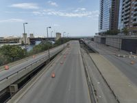 several road construction work on an empty highway near some tall buildings and a bridge over the water