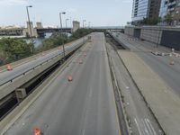 several road construction work on an empty highway near some tall buildings and a bridge over the water