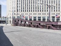 a metal bridge over a brick street with buildings behind it and an american flag at the end