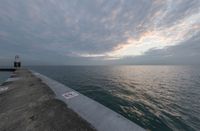 an overcast sky above the ocean as seen from a concrete dock with a lighthouse