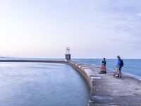 a man riding on a bicycle down the side of a pier near a light house