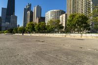 a young boy skateboarding on the cement in an empty city park as a skyscraper is built in background