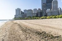 an empty sandy beach with many large buildings in the background in the foreground is the river and sand