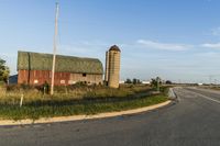 a rural country road leading to a barn and grain silo at the intersection of a street