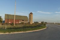 a rural country road leading to a barn and grain silo at the intersection of a street