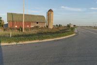 a rural country road leading to a barn and grain silo at the intersection of a street