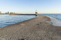 a beach near some water with a light post at the end of the pier in the middle of the sand