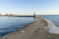 a beach near some water with a light post at the end of the pier in the middle of the sand