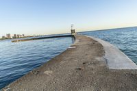 a beach near some water with a light post at the end of the pier in the middle of the sand