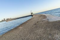 a beach near some water with a light post at the end of the pier in the middle of the sand