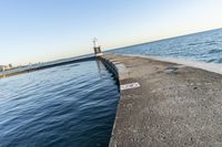 a beach near some water with a light post at the end of the pier in the middle of the sand