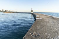 a beach near some water with a light post at the end of the pier in the middle of the sand