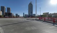 the empty parking lot of a city next to tall buildings in the background with many cars driving along