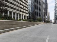 the man rides his skateboard along the side of a street in tall buildings on a sunny day