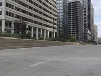 the man rides his skateboard along the side of a street in tall buildings on a sunny day