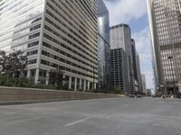 the man rides his skateboard along the side of a street in tall buildings on a sunny day