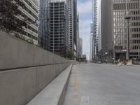 the man rides his skateboard along the side of a street in tall buildings on a sunny day