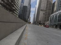 the man rides his skateboard along the side of a street in tall buildings on a sunny day