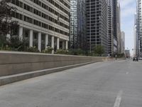 the man rides his skateboard along the side of a street in tall buildings on a sunny day