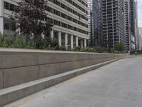 the man rides his skateboard along the side of a street in tall buildings on a sunny day