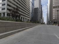 the man rides his skateboard along the side of a street in tall buildings on a sunny day