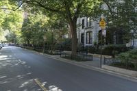 people walking down the sidewalk on a sunny day in an empty street of buildings, in an area with trees, bushes and a fence