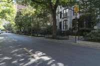people walking down the sidewalk on a sunny day in an empty street of buildings, in an area with trees, bushes and a fence
