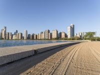 sand covering the ground next to the water near some buildings with trees in the background