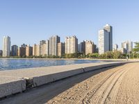 sand covering the ground next to the water near some buildings with trees in the background