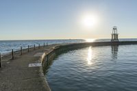 an empty pier next to the ocean with a sun shining above it and a lighthouse on a sunny day