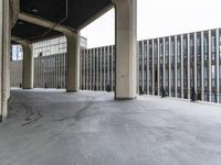 large concrete buildings with columns in an outdoor space under a bridge that extends the city across the river