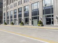 a sidewalk near a large commercial building with two green planters in the street outside